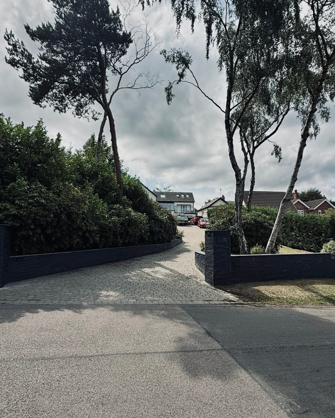 A block-paved driveway with slate boundary walls and silver birch trees in daylight