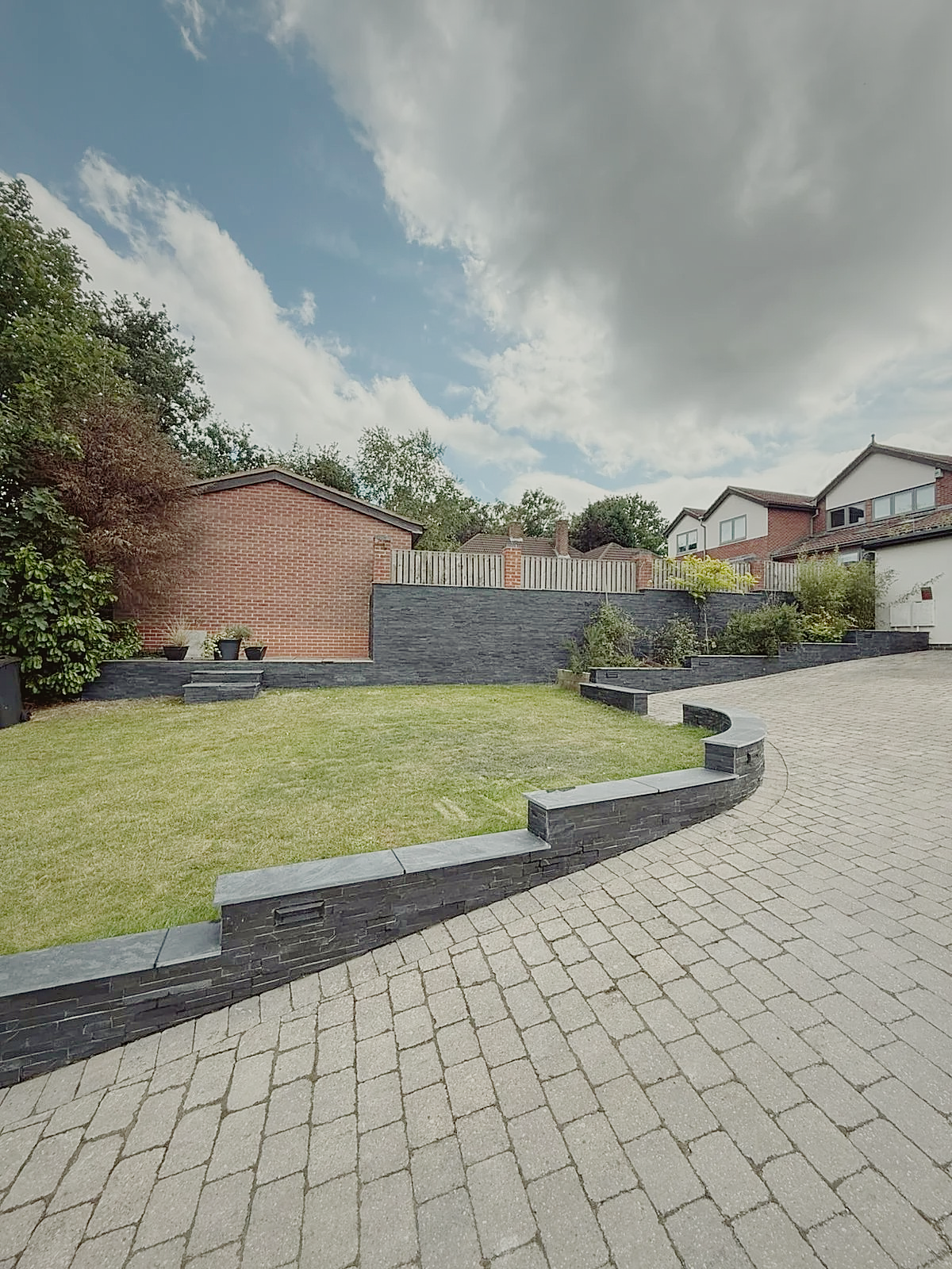 A terraced front garden with slate walls meeting a block-paved driveway