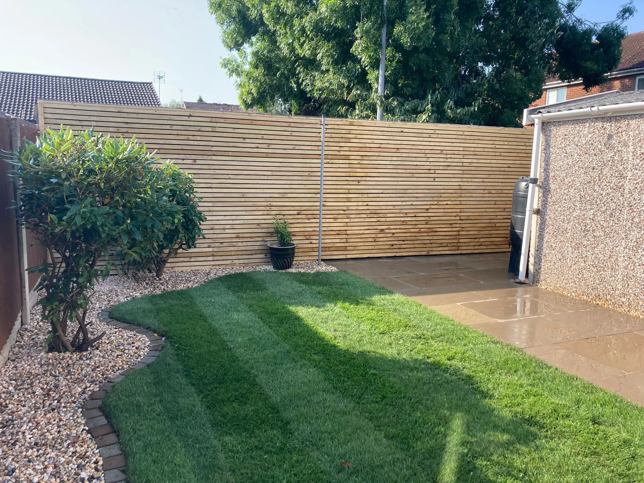 A freshly striped lawn with slatted fencing and clean sandstone paving