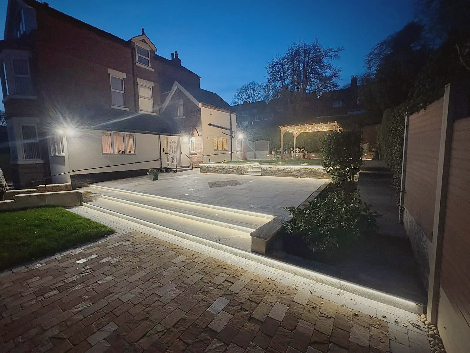 A terraced garden with lit floating steps and a pergola at blue hour
