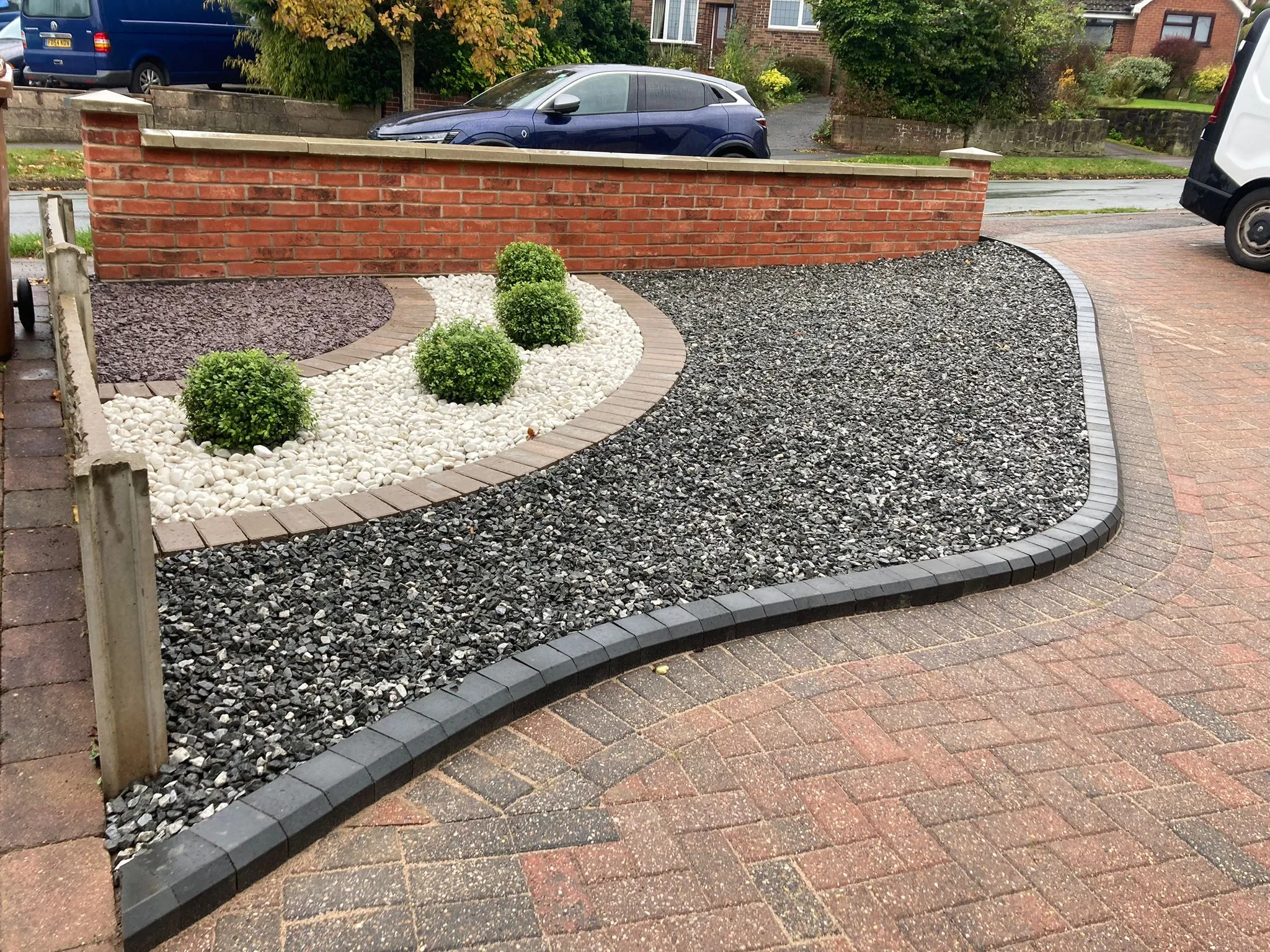 A front garden with layered gravel beds, box planting and block paving with charcoal edging
