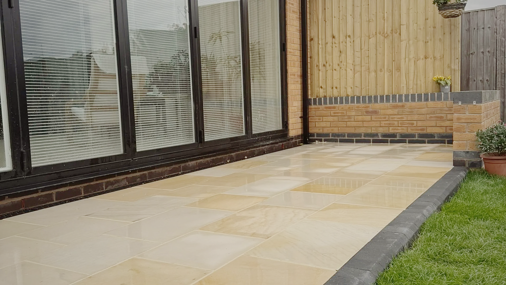 A sandstone patio with charcoal edging against black-framed bifold doors